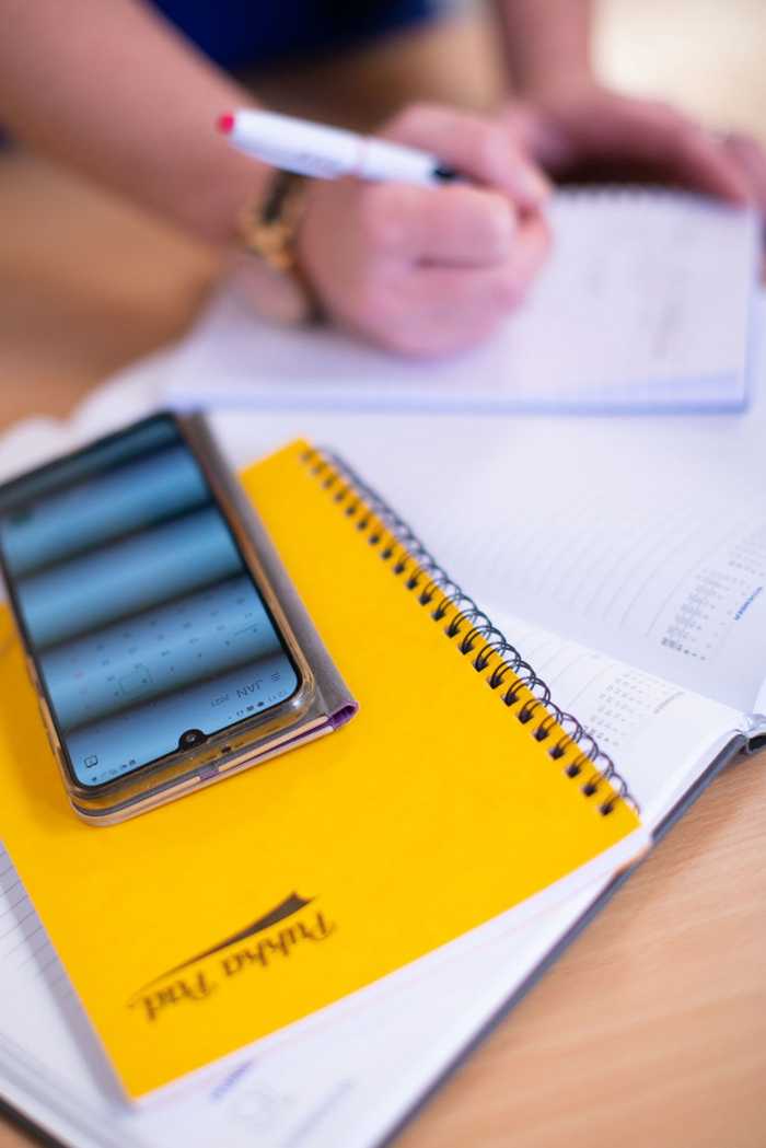 Lady writing on a notepad with while using smartphone calendar