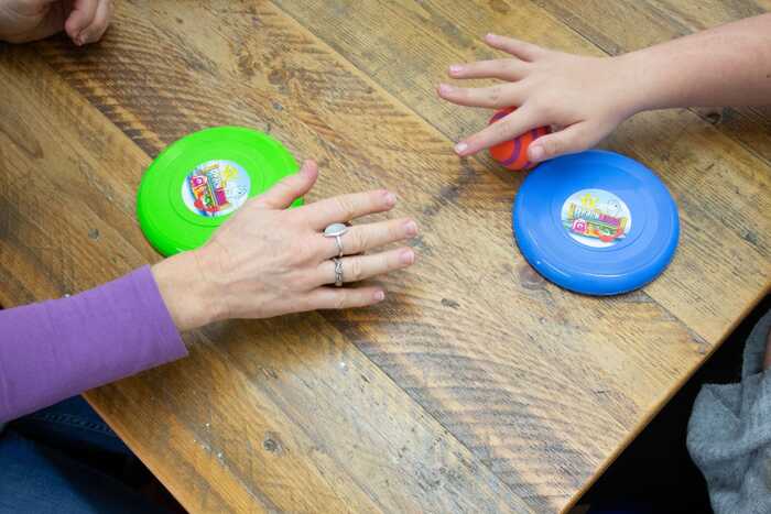 Two hands reaching for green and blue disks on a wooden table.