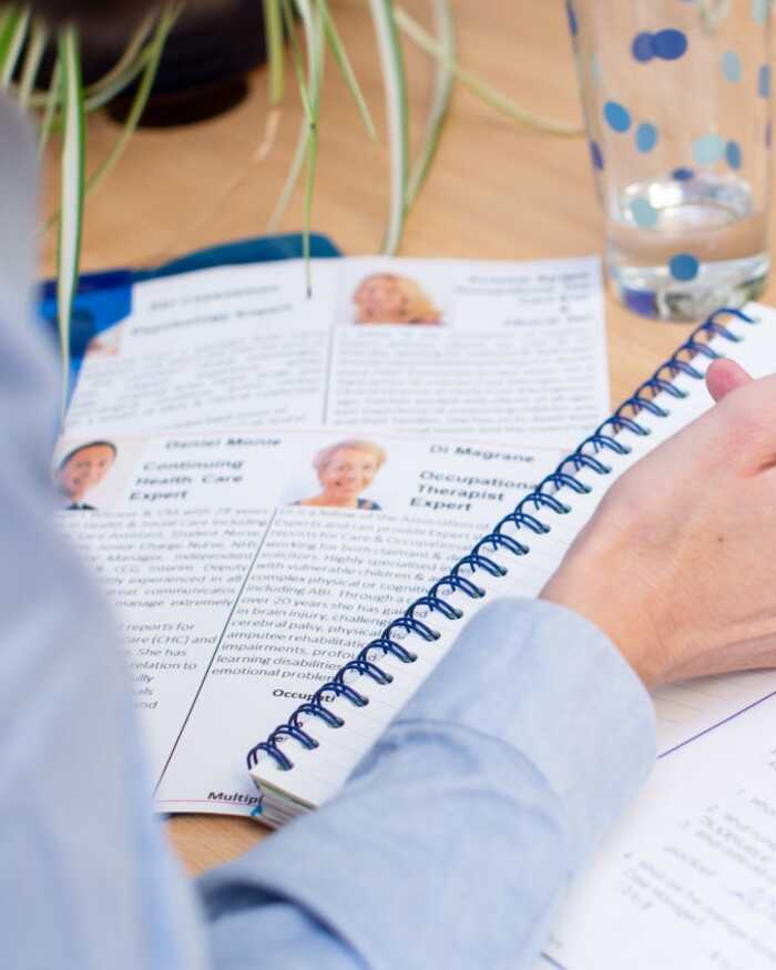 A person writes in a notebook, surrounded by documents and a glass of water.