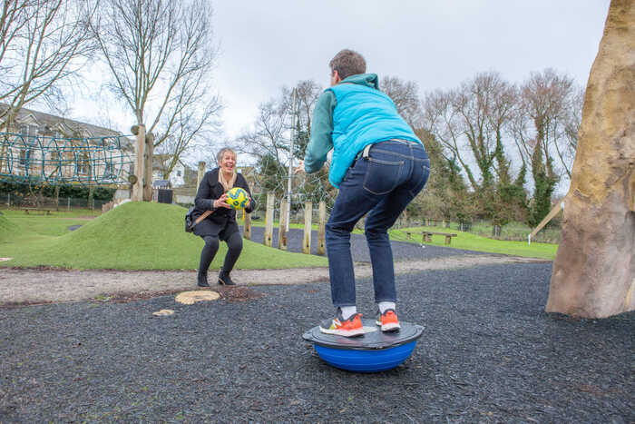 Children playing on playground equipment, one balancing and the other throwing a ball.