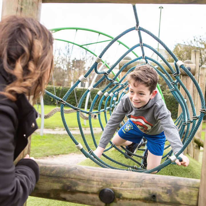 A boy plays on a climbing structure while a woman watches him from the side.