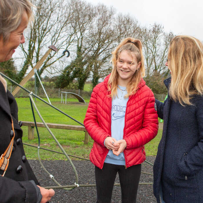 Three people talk together at a playground, with trees in the background.